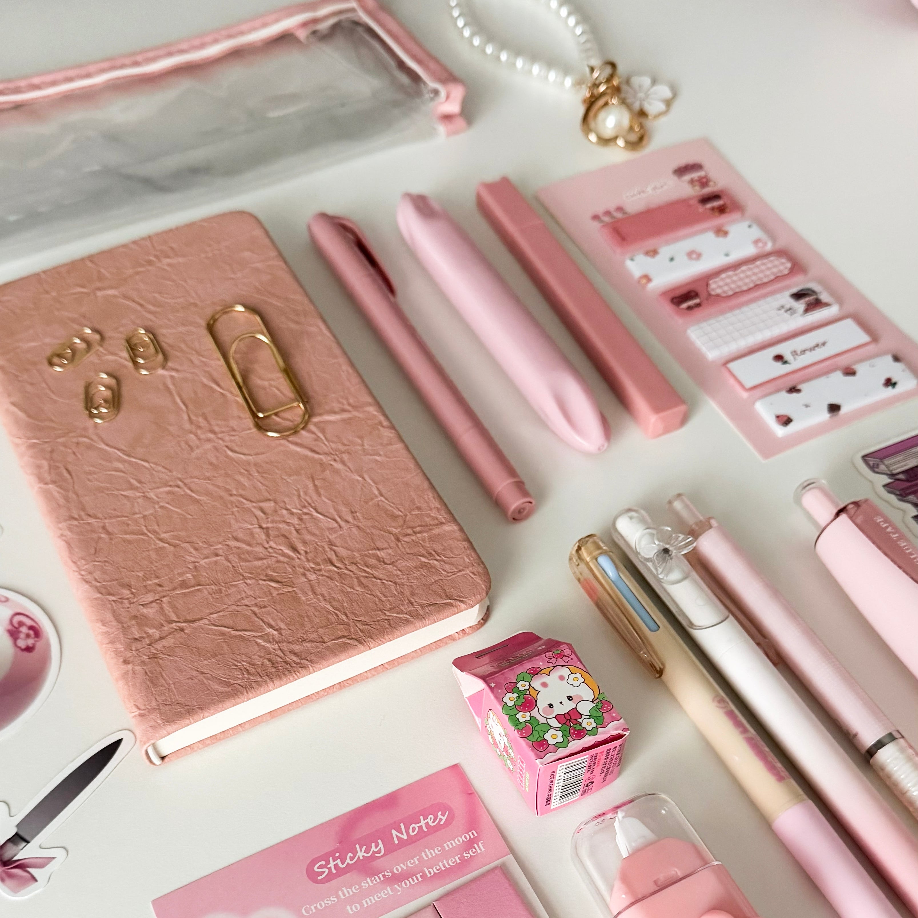 Close-up of a pink bookish stationery gift bundle with notebook, pens, pencil pouch, sticky notes, correction tape, bookmarks, and aesthetic desk accessories.