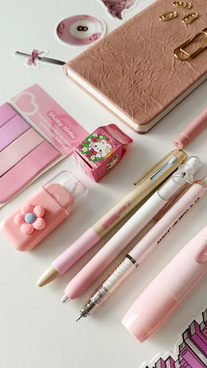 Close-up of pink stationery accessories featuring notebook, gel pens, correction tape, sticky notes, eraser, and cute desk essentials from a pink stationery gift bundle.