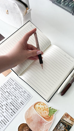 Writing with a coffee-themed gel pen in a cream notebook from the Morning Coffee Stationery Gift Bundle, featuring cozy aesthetic stationery for book lovers and journal enthusiasts.