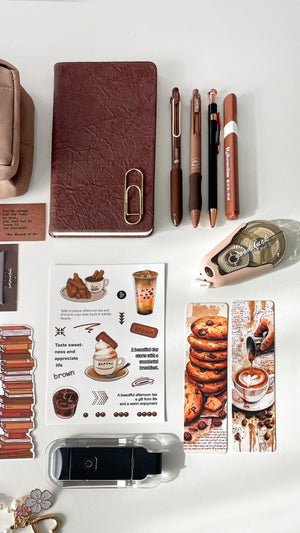 Close-up of a premium coffee stationery gift bundle featuring a coffee latte memo pad, coffee-themed stickers, bookmarks, LED reading light, and pearl keychain charm.