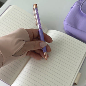 Writing with a luxury purple pen from the Essential Purple Stationery Gift Set beside an open notebook and lavender pencil pouch