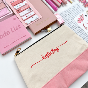 Cream and pink Bestie canvas pencil pouch with gold zipper, surrounded by coordinating pink notebooks and journaling stationery.