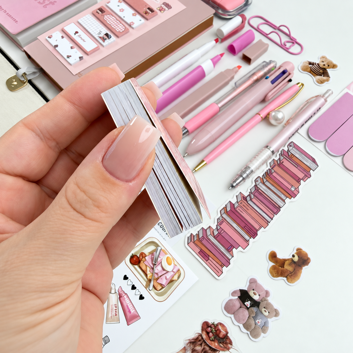 Side view of a mini collage materials booklet showing its stack of tear-out decorative pages beside pink stationery and stickers.