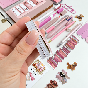 Side view of a mini collage materials booklet showing its stack of tear-out decorative pages beside pink stationery and stickers.