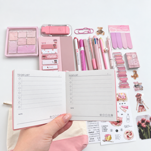Open pink to-do notebook showing checklist pages and note sections, with matching pink stationery and journaling accessories in the background.