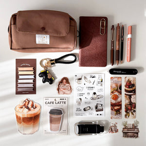 A styled flat-lay of coffee-themed stationery and accessories on a white background, including a brown cosmetic pouch, a brown leather wallet, pens, stickers, a keychain, and coffee latte illustrations.