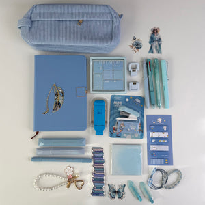 A flat lay of coordinated stationery and desk accessories in pastel blue tones on a white background, including a striped blue pencil case, notebook, pens, sticky notes, clips, a mini stapler, and decorative accessories.