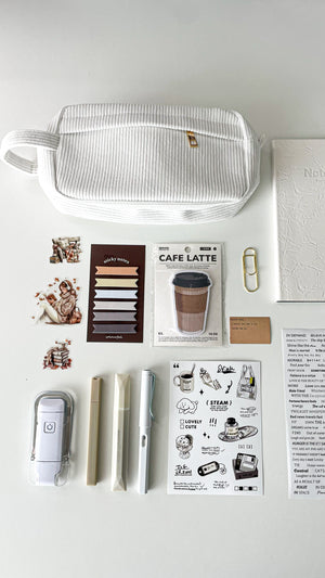 Close-up of the Morning Coffee Stationery Gift Bundle featuring a cream corduroy pencil pouch, latte memo pad, sticky notes, LED reading light, cream notebook, coffee-themed stickers, and journaling accessories.