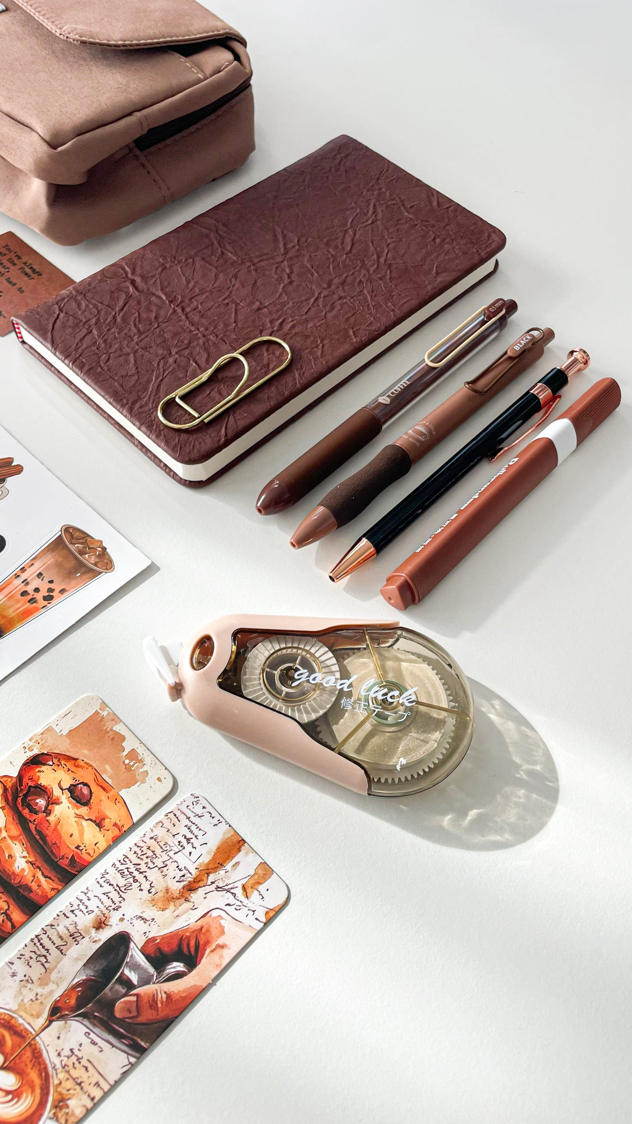 Close-up of a premium coffee stationery gift bundle featuring a premium pencil pouch, A6 notebook, black and gold metal pen, coffee gel pens, acrylic marker, and gold paperclip bookmark.