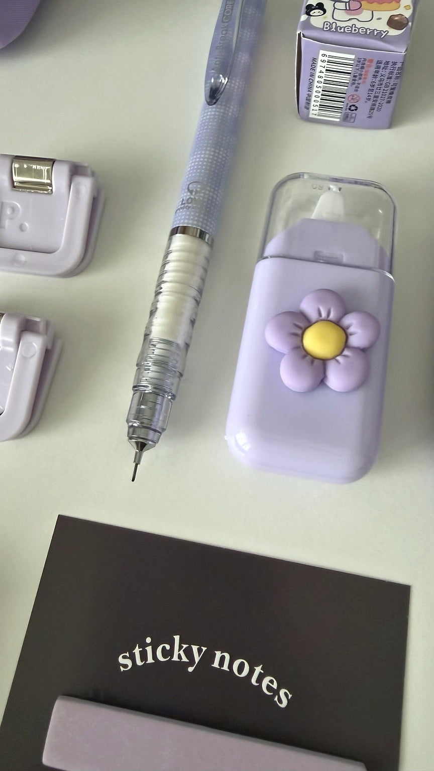 Close-up of pastel stationery accessories included in the Essential Purple Stationery Gift Box, featuring a mechanical pencil, flower eraser, sticky notes, and binder clips
