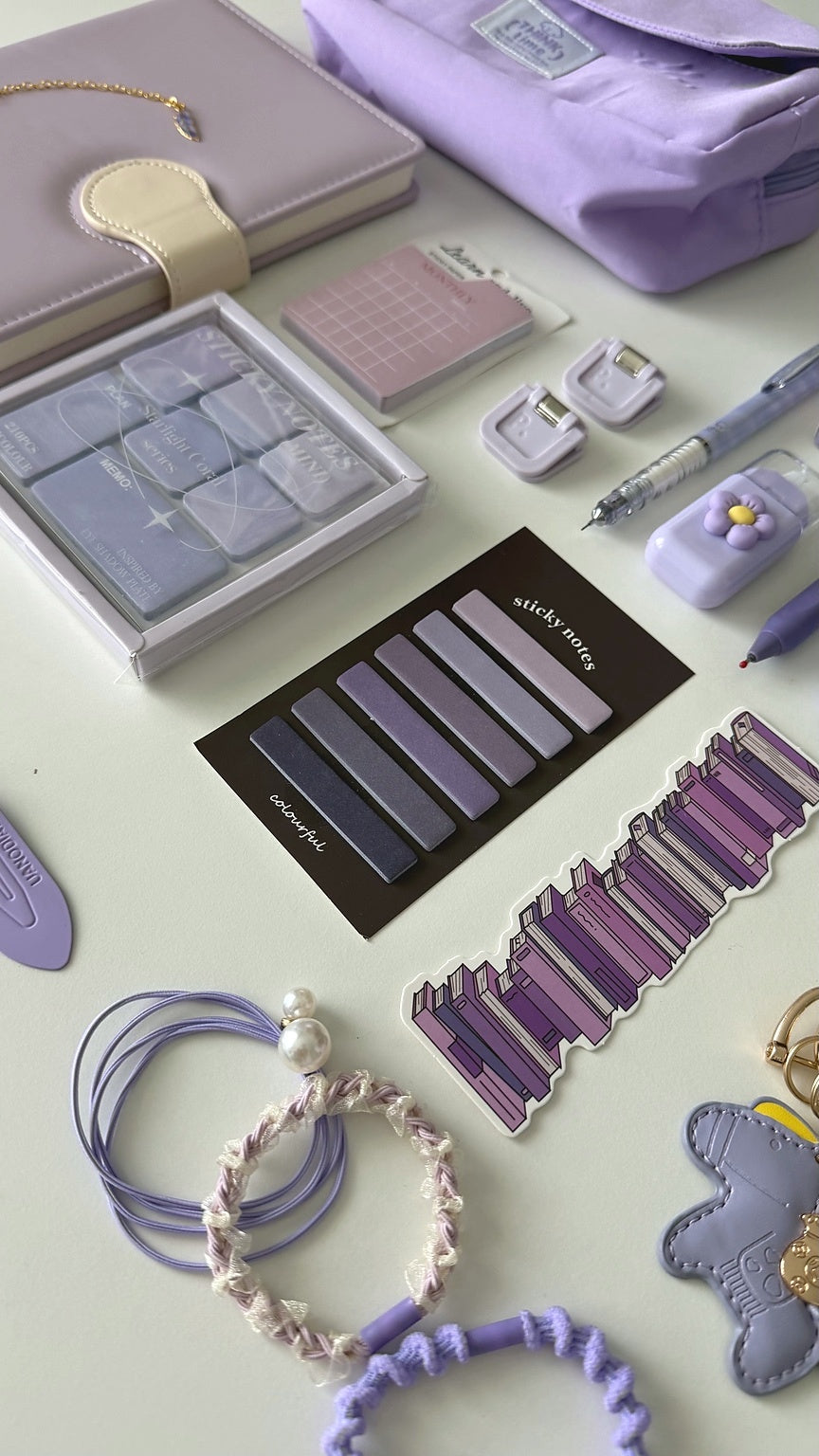 Close-up of pastel stationery accessories from the Essential Purple Stationery Gift Set featuring sticky notes, bookmarks, planner accessories, hair ties, and a keychain